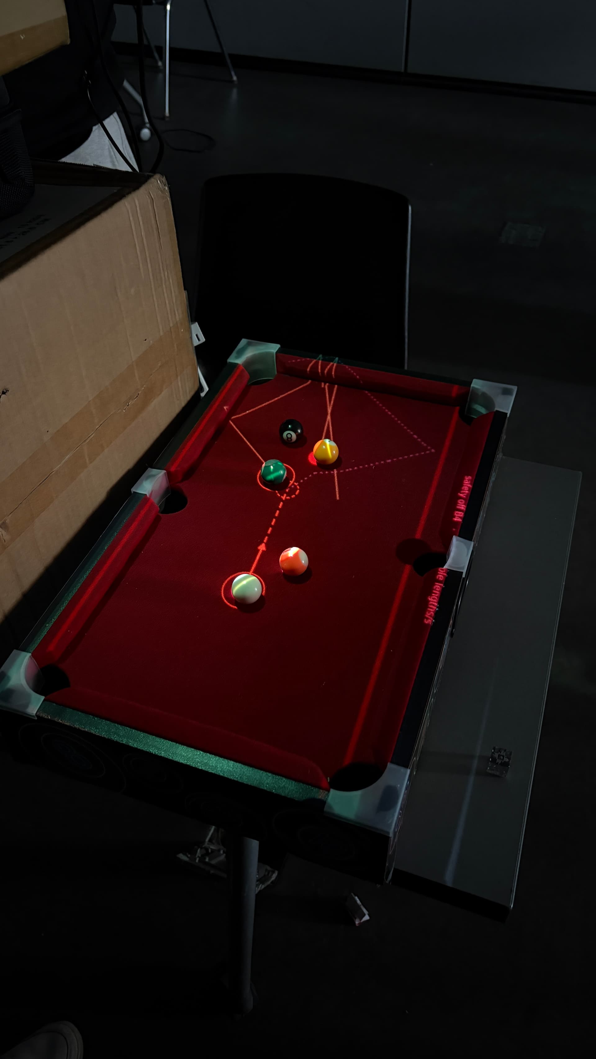 Otli projecting shot-guidance lines directly onto a mini pool table in the dark